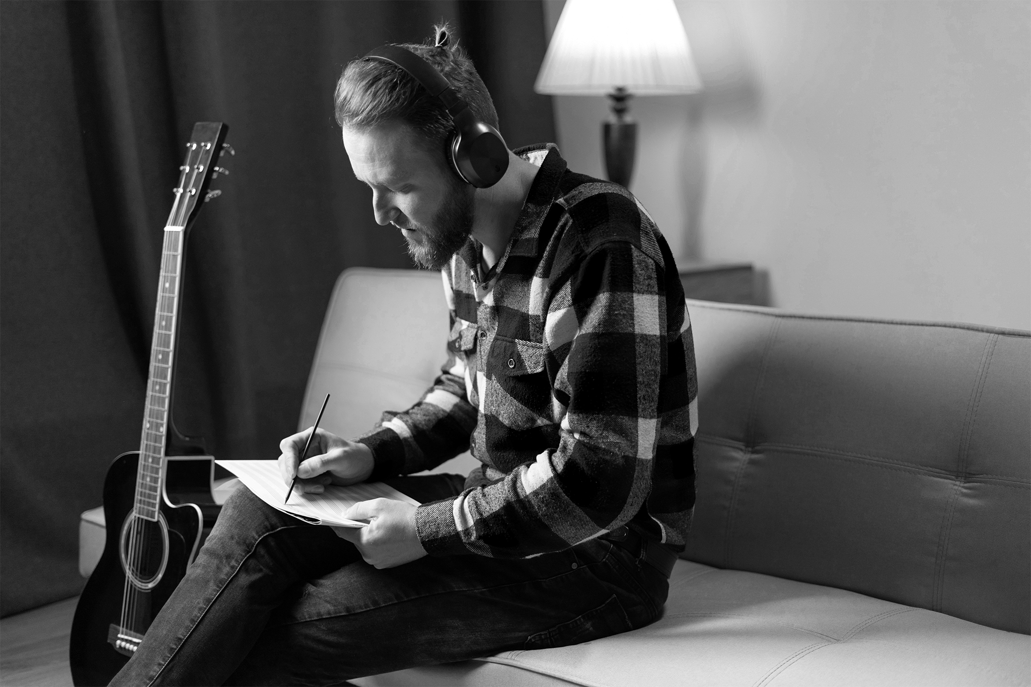 Man sitting on couch writing song with guitar next to him